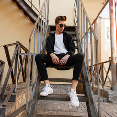 Stylish young hipster man in trendy sunglasses in a black shirt in a t-shirt in elegant striped...