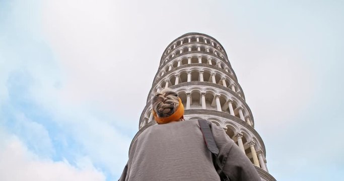 Upward view of tourist girl looking at stunning Leaning Tower famous landmark. Back of young woman standing against tourist attraction in Piazza dei Miracoli. Pisa, Tuscany, Italy
