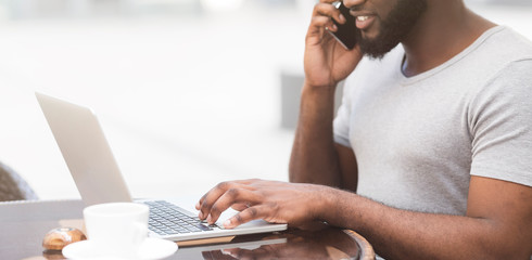 African american man typing on laptop and talking on cellphone