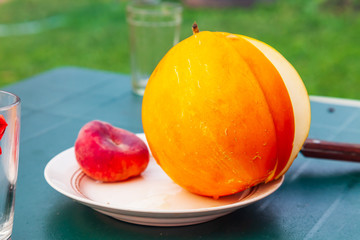 Fresh yellow melon with a cut off piece is lying on a white plate on the table. Fruits and vitamins for health and benefits.