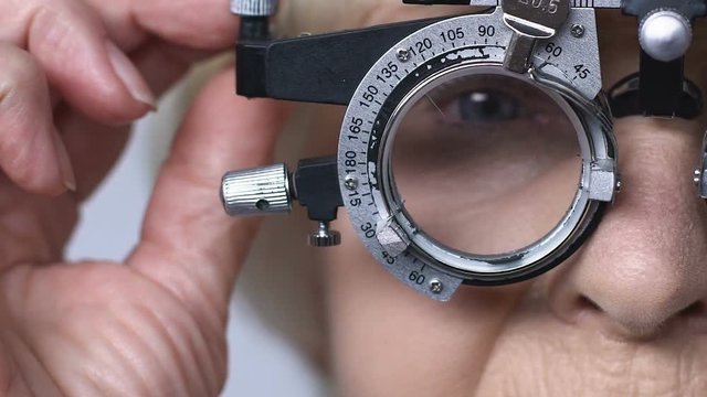 Old woman taking off optical trial frame with lens, blurry vision, presbyopia