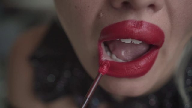 Close-up of a seductive blonde woman, carelessly putting on red lipstick. Makeup, sexy blonde unevenly puts red lipstick on her lips.