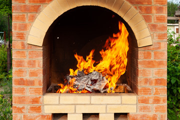 Obraz premium Brick stove in the yard with large flames from the fire in preparation for cooking meat in the open air on a warm summer day.