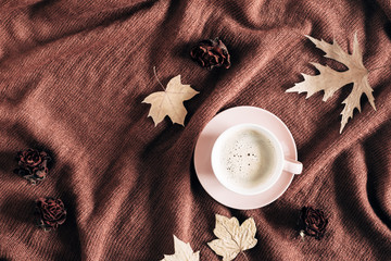 Autumn home cozy composition. Cup of coffee, knitted plaid, dried autumn leaves on brown...