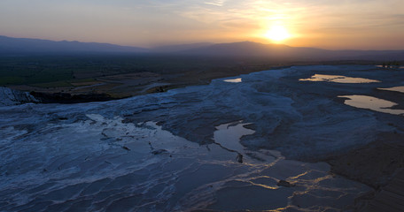 Fototapeta premium Turkey, sunset on the travertine terraces at Pamukkale (Cotton Castle), natural site of sedimentary rock deposited by water from the hot springs, famous for a carbonate mineral left by flowing water