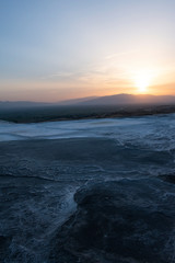 Fototapeta premium Turkey, sunset on the travertine terraces at Pamukkale (Cotton Castle), natural site of sedimentary rock deposited by water from the hot springs, famous for a carbonate mineral left by flowing water