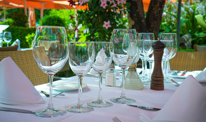 Close up white empty plates wine glasses, wooden table setting at home in outdoors terrace, plant on weave pot no people.