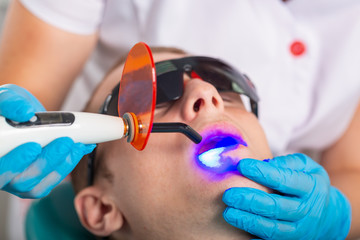 Close-up portrait of a male patient at dentist in the clinic. Teeth whitening procedure with ultraviolet light UV lamp.