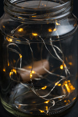 Decorative lights in glass jar at the dark room with mirror effect on dark background. Festive decorations .Warm white led lights.