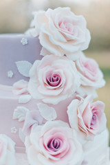 Close-up of parts of a three tiered wedding cake in pastel colors decorated with realistic pink roses on a blurred background of the garden, selective focus