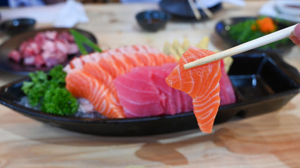 Salmon sashimi slice on chopsticks.