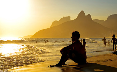 silhouette of a man sitting on the beach at sunset