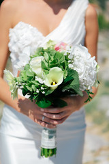 The bride is holding a bouquet of fresh spring and summer flowers in pastel colors on a blurred background, selective focus