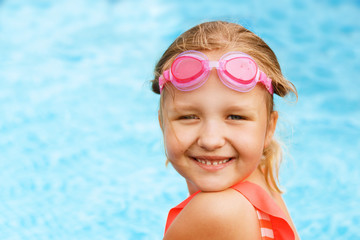 Charming little girl swims in the pool. A child with glasses smiles and looks into the camera.