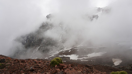 Large clouds swim through the gorge. Mountainous area. Snow is visible on the mountain slopes. Green moss grows on the stones. Hiking in the mountains. Snowy peak.