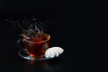 A cup of black tea on a black isolated background. Meringue next to the cup. Testy dessert. Splash