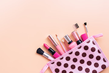 A variety of cosmetics for women's makeup in a cosmetic bag on a pastel pink background. Top view, flat lay, copy space.