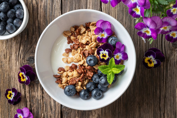 Obraz na płótnie Canvas Breakfast cereals with yogurt, blueberries and pansies