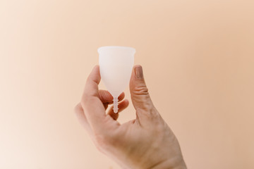 hand holding a menstrual cup in front of a peach background