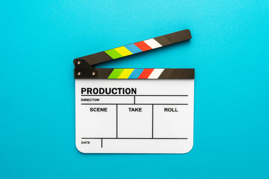 Top view photo of open white clapperboard over turquoise blue background. Flat lay image of blank acrylic movie clapboard. Central composition of movie clapper as filmmaking concept.