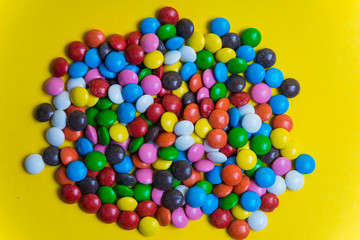 Colorful background of multicolored candy dragees. Round  scattered sweets on a yellow bright background. Happy multicolor texture. Sweet candy wallpaper. Shallow depth of field. Flat lay on surface
