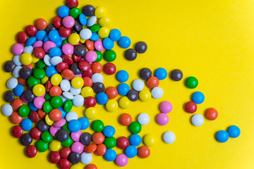 Colorful background of multicolored candy dragees. Round  scattered sweets on a yellow bright background. Happy multicolor texture. Sweet candy wallpaper. Shallow depth of field. Flat lay on surface