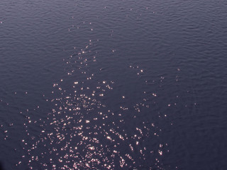 Bright small sunny highlights on the dark purple water of the lake background.