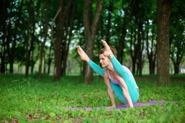 Thin brunette girl plays sports and performs beautiful and sophisticated yoga poses in a summer...