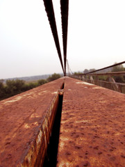 Old red iron stripes of the handrail, steel cables, construction of a metallic rusty bridge.
