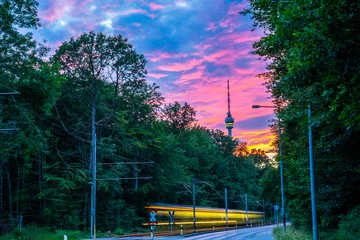 Deutschland, Stuttgarter Stadtfernsehturm im grünen Wald mit leuchtendem Himmel nach Sonnenuntergang von der Straße mit Straßenbahnverkehr in der wunderschönen Naturlandschaft des umliegenden Waldes © Simon Dux Media
