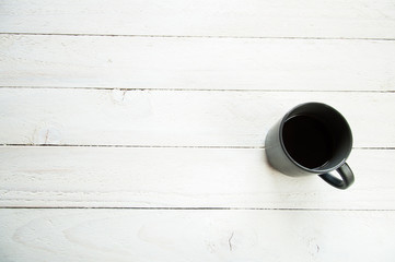 Black cup with coffee on the white table. White wooden background. Board of boards