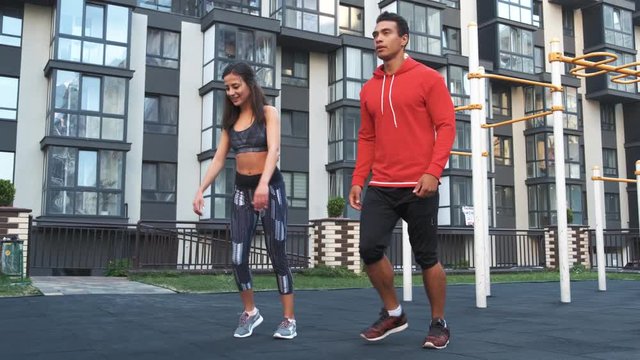 Image of young sporty man and woman 20s in tracksuits doing workout and squatting together