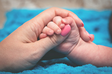Mom and baby hold hands together on a blue background.