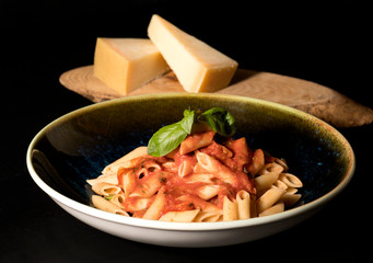 Homemade pasta with tomato sauce in a black plate on a black table served with kashar cheese on a wooden cutting board_3
