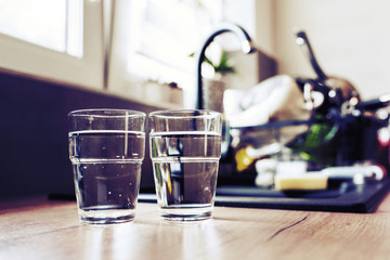 Two glasses of water in kitchen, with tap water and two bottles of mineral water. Shallow depth of field. Water shortage concept, saving water. Body hydration with clean & clear water.