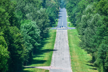Long asphalt straight road through the forest. Road with ups and downs. Sunny and cloudy day.