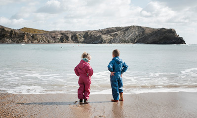Siblings wearing raincoat standing on beach