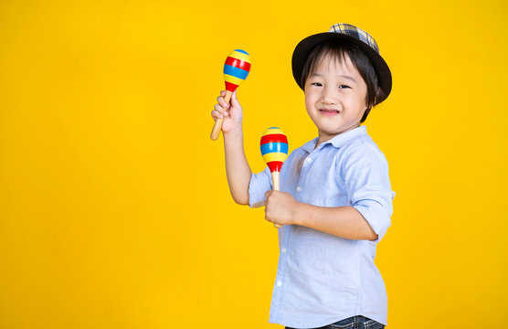 Portrait of little cute asian boy playing the maracas isolated on yellow background, preschool play group, music learning by doing and education concept
