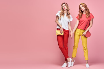 Fashionable embracing woman sisters smiling on pink background. Two Shapely Girl Having Fun dance, Trendy yellow coral summer outfit, fashion hairstyle, makeup. Gorgeous female model, funny concept