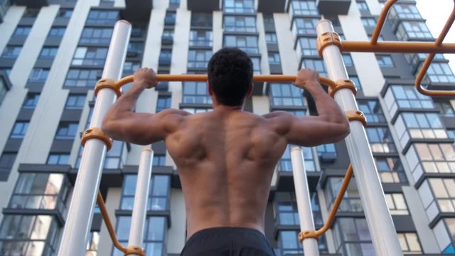 Muscular man doing pull-ups on horizontal bar. on workout area near house.