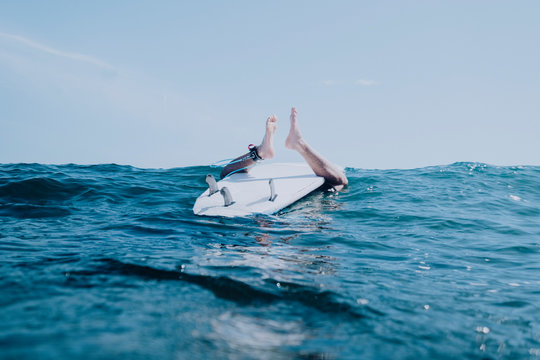 A surfer sits on board upside down on water surface