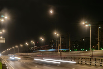 The moon rising over the illuminated highway and the night city,