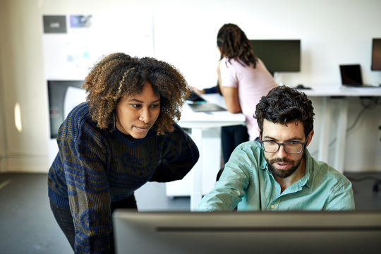 High angle view of businessman explaining to businesswoman over desktop computer in office
