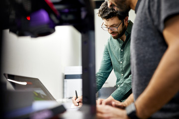 Businessman writing while standing with male colleague in office