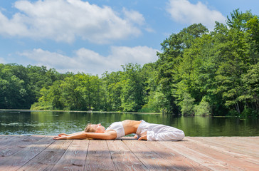Attractive woman is practicing yoga and meditation in Supta Virasana pose near lake in morning.