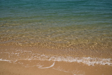 Tropical shore with yellow clean sand and light blue water in the sun