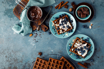 Chocolate belgian waffles with ice cream and fresh blueberry on blue background, top view