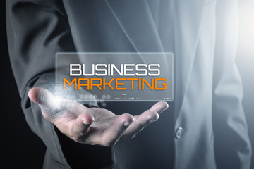 Hand holding transparent screen with text BUSINESS MARKETING