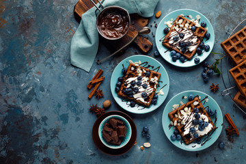 Chocolate belgian waffles with ice cream and fresh blueberry on blue background, top view
