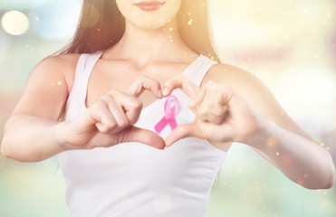 Heart framing from fingers on woman chest with pink badge to support breast cancer cause, PS: you...